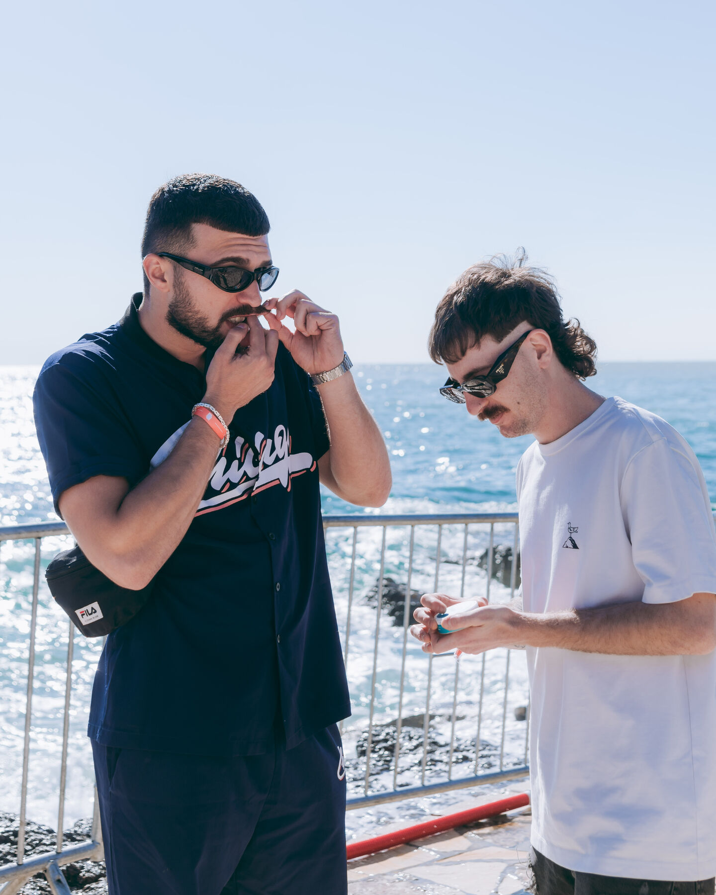 Zwei Männer mit Sonnenbrillen stehen am Meer und benutzen skruf.-Dosen.