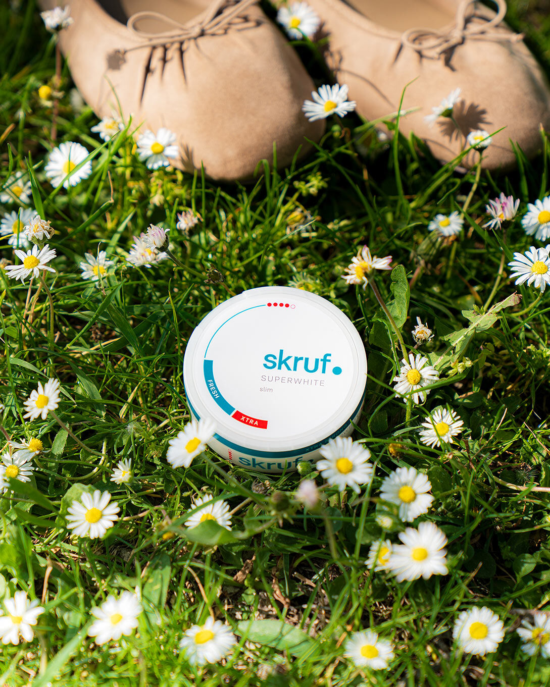 Dose mit skruf Slim Pouches liegt im Gras zwischen Gänseblümchen.