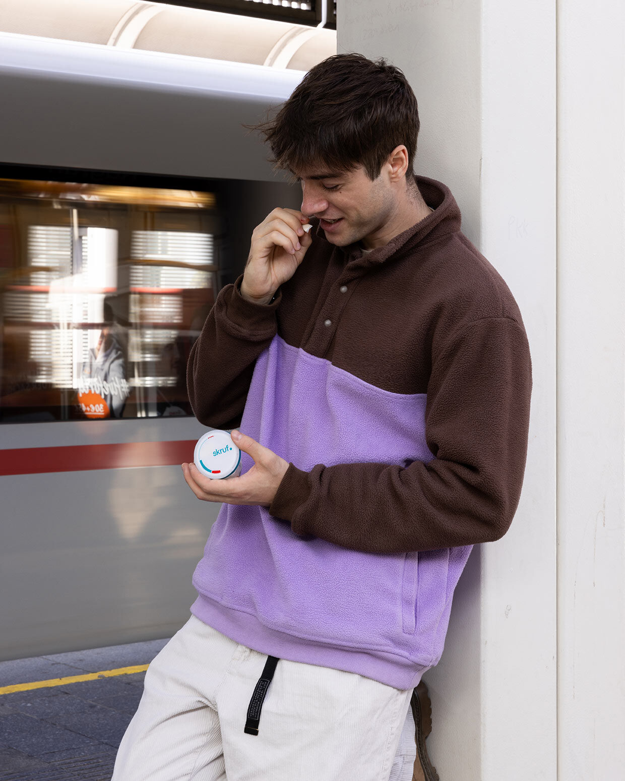 Junger Mann hält eine skruf Dose und einen weißen Nikotinbeutel neben einer Zugtür.