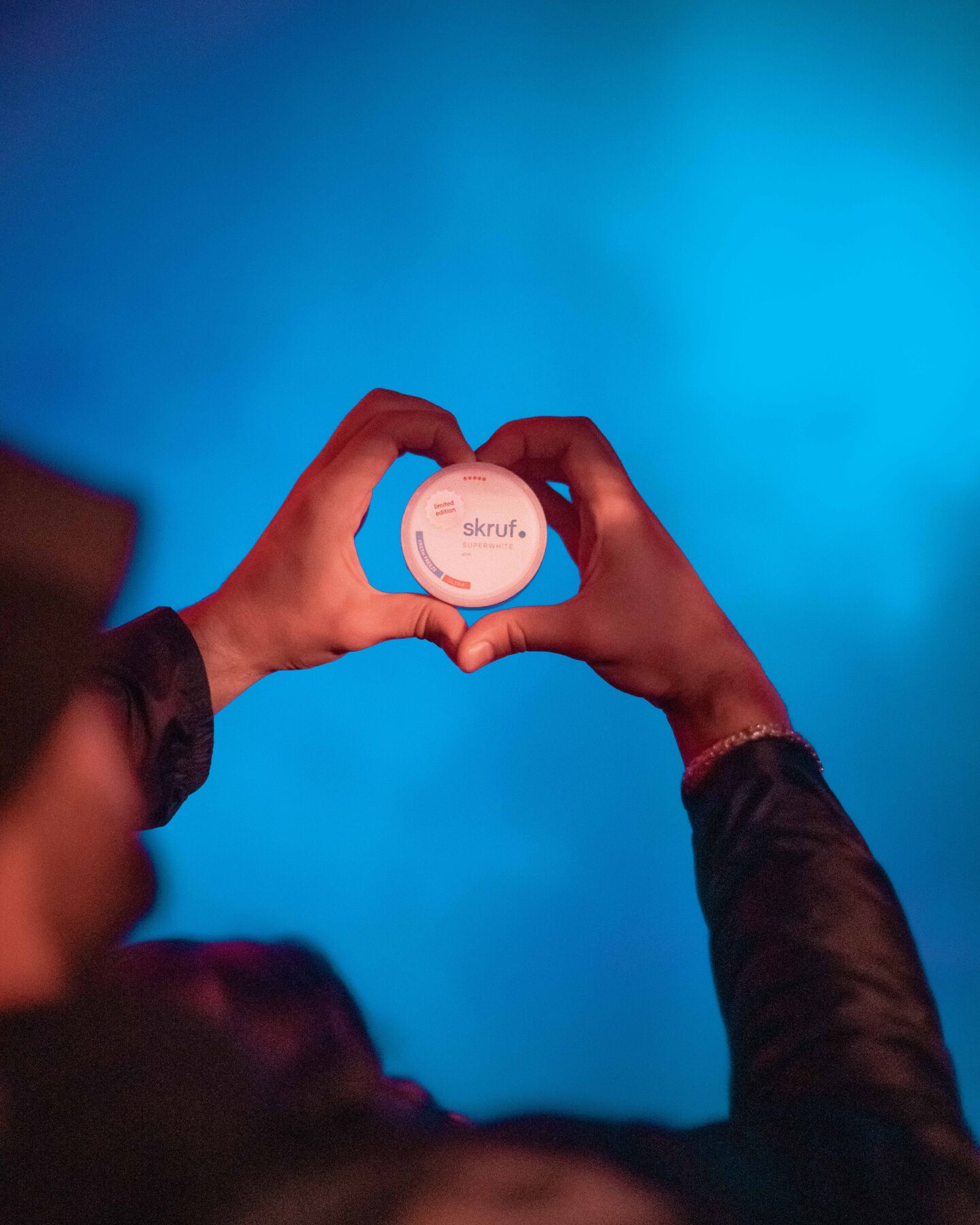 Hände formen Herz um weiße skruf.-Dose vor blauem Licht.