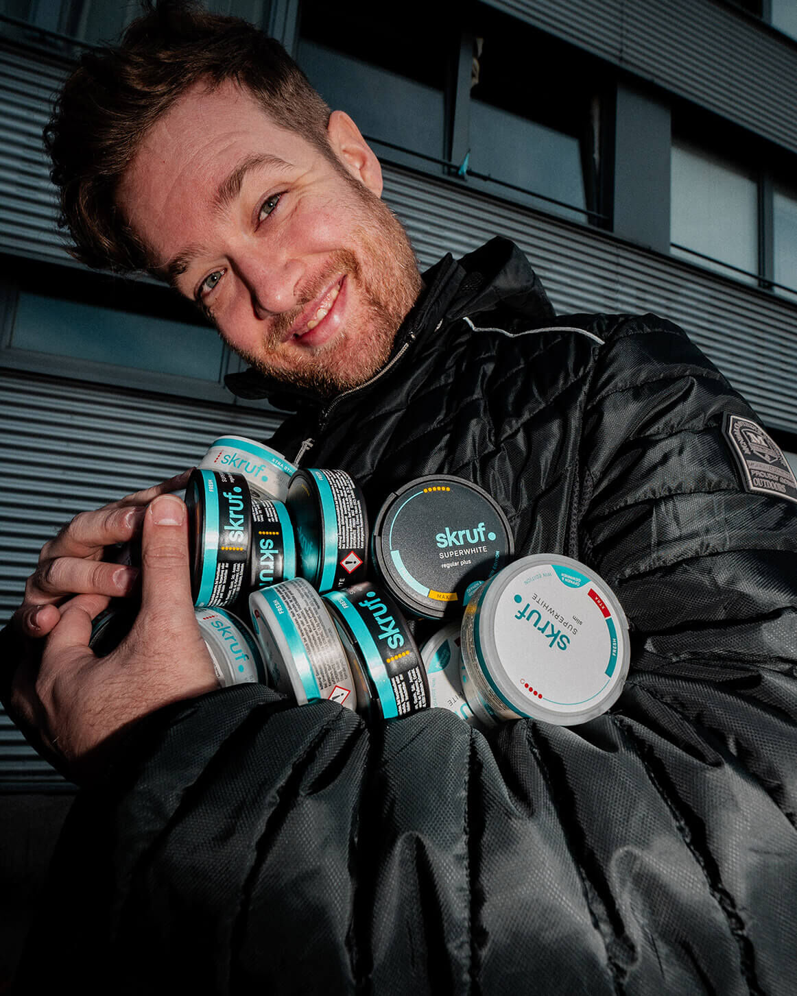 Mann hält mehrere skruf Nikotinbeutel-Dosen im Arm.