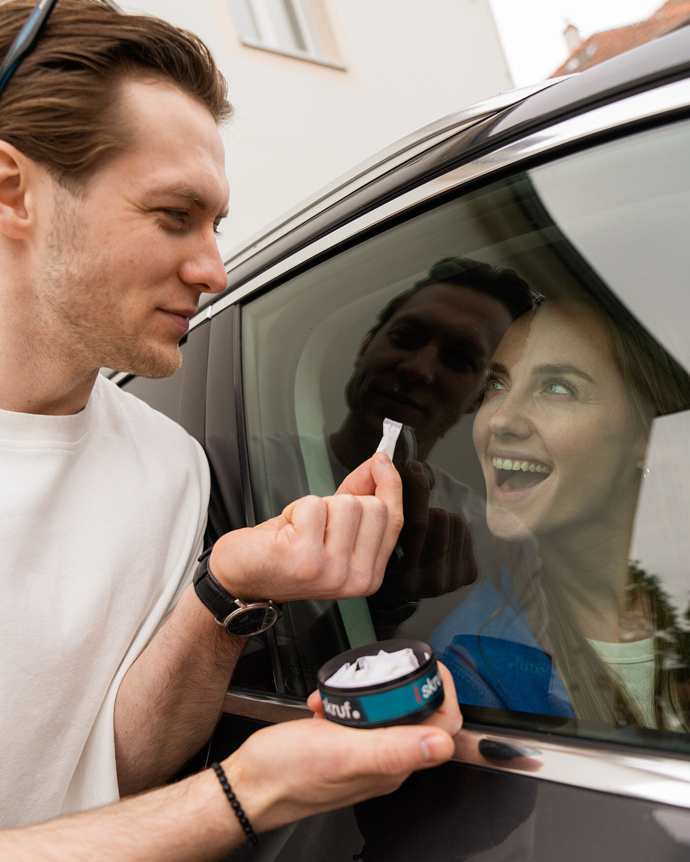 Mann hält einer Frau in einem Auto eine skruf Dose hin.