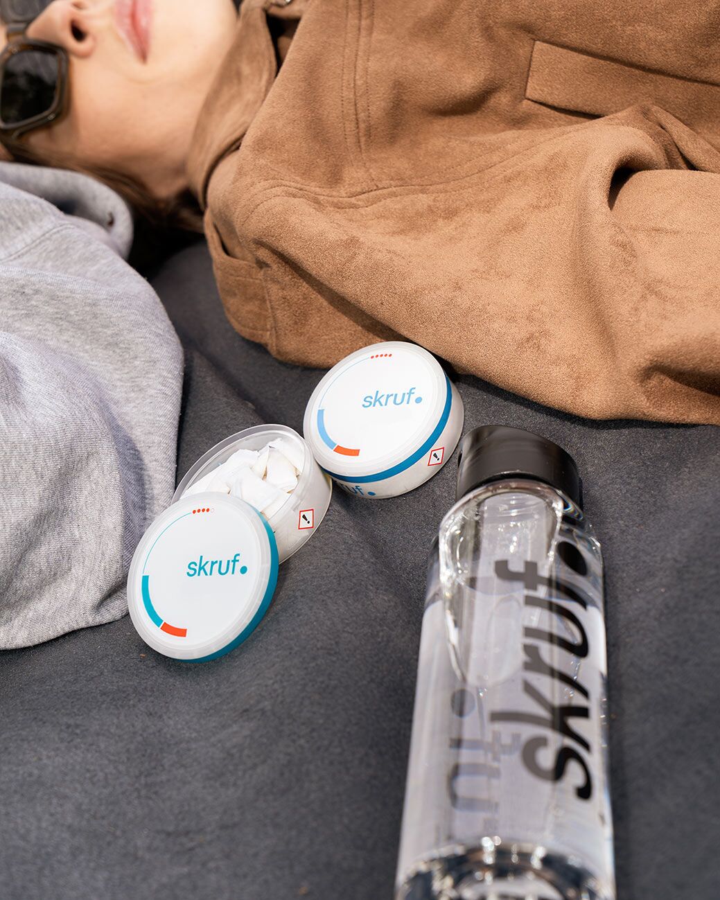Slim Pouches und Trinkflasche liegen neben zwei Personen auf einer Decke.