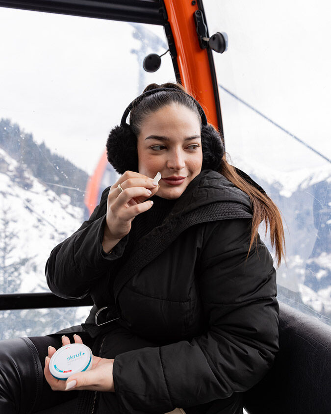 Frau in der Gondel mit schwarzen Ohrenwärmern hält eine skruf Nikotinbeutel in der einen, eine Dose in der anderen Hand