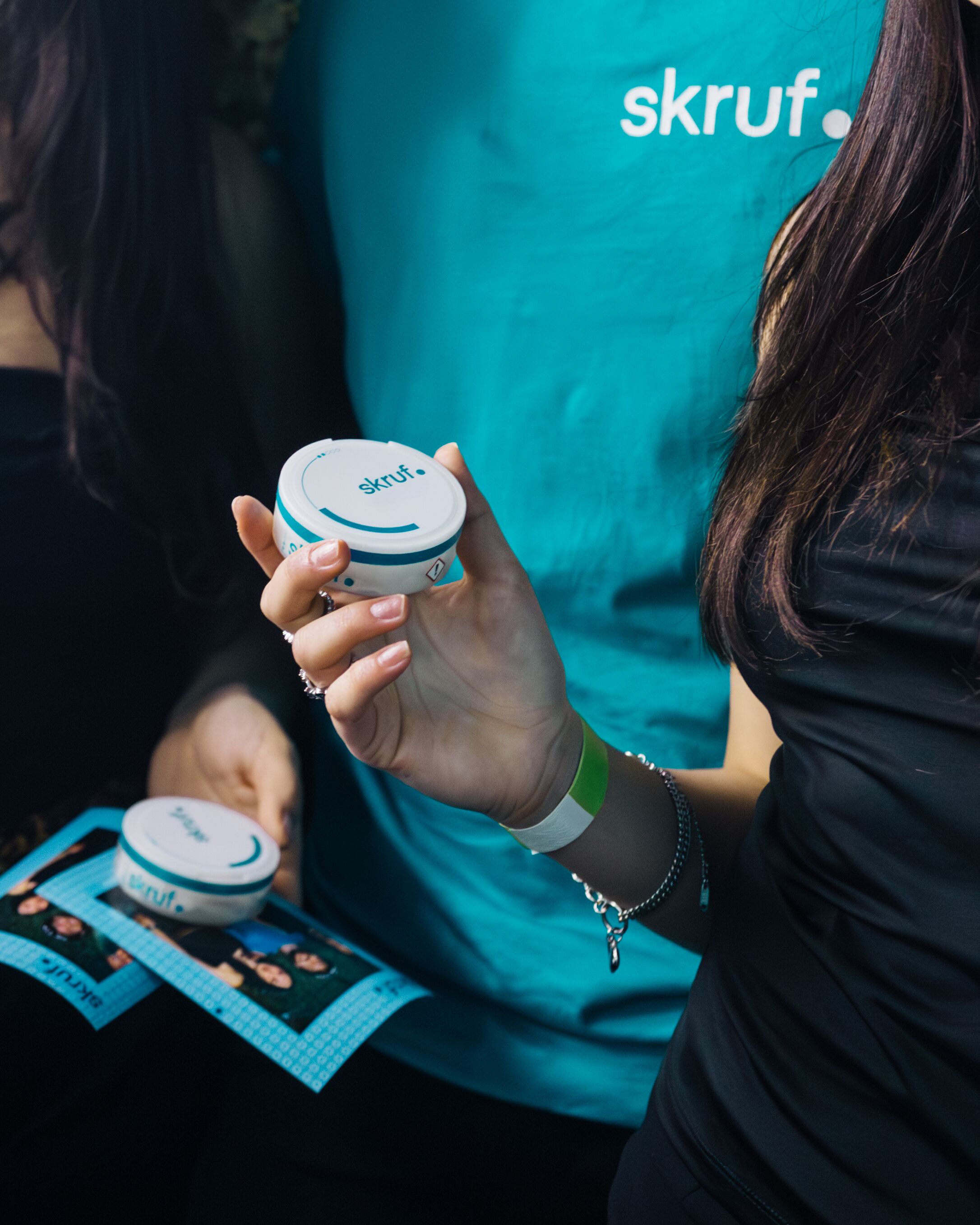 Person hält eine skruf-Dose in der Hand, während im Hintergrund weitere Personen und ein skruf-Branding auf einem Event zu sehen sind.