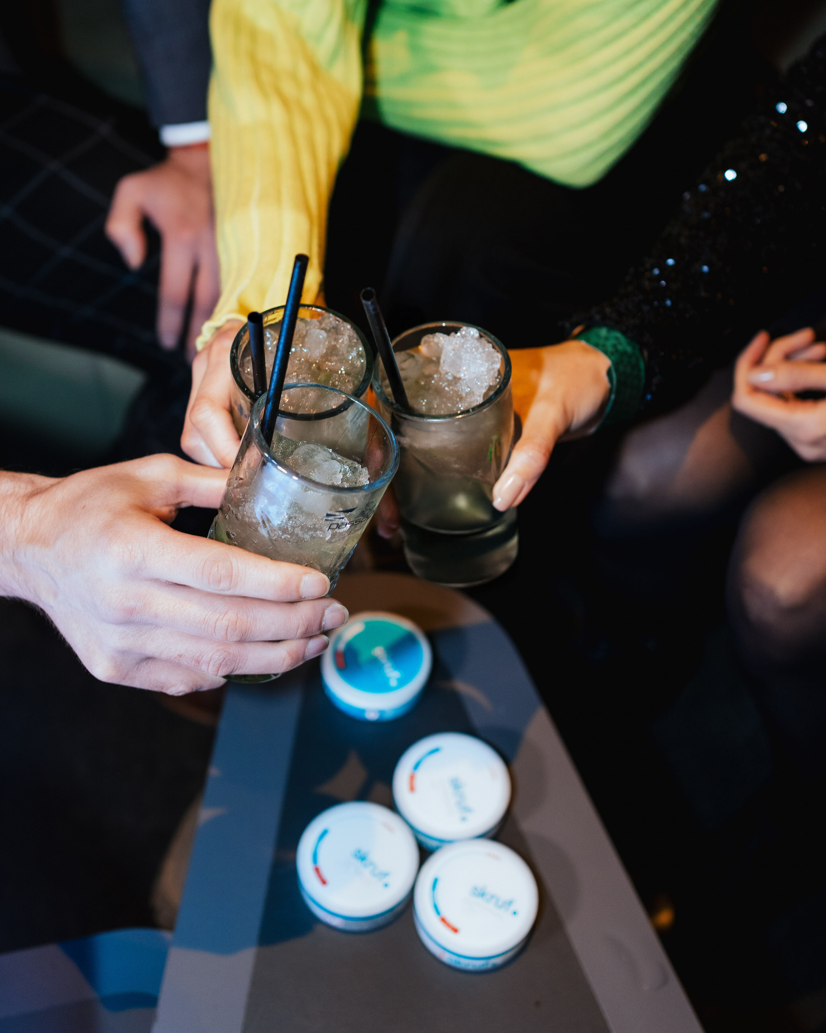 Drei Freunde stoßen mit eisgekühlten Cocktails und frischer Minze an; im Vordergrund auf dem Tisch liegen vier skruf Superwhite Dosen bereit.