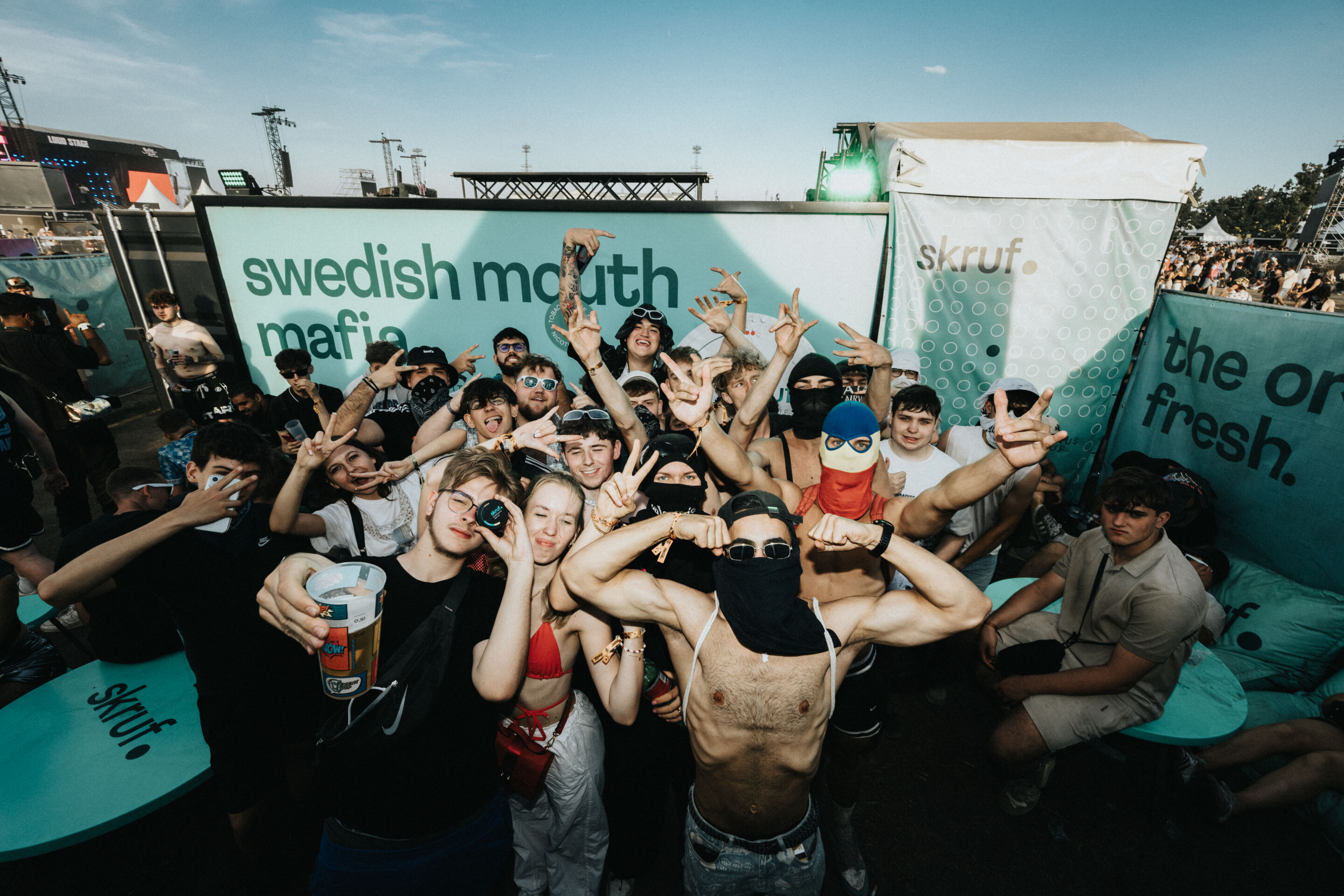 Große feiernde Gruppe vor skruf.- und „swedish mouth mafia“-Bannern auf einem sommerlichen Festival.