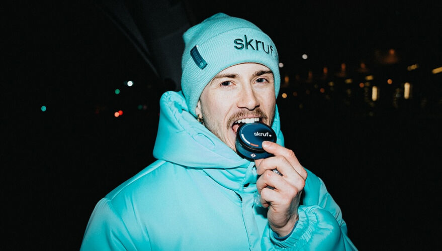 Person mit hellblauer Mütze und Jacke hält eine skruf-Dose vor den Mund. Nachtaufnahme mit dunklem Hintergrund.
