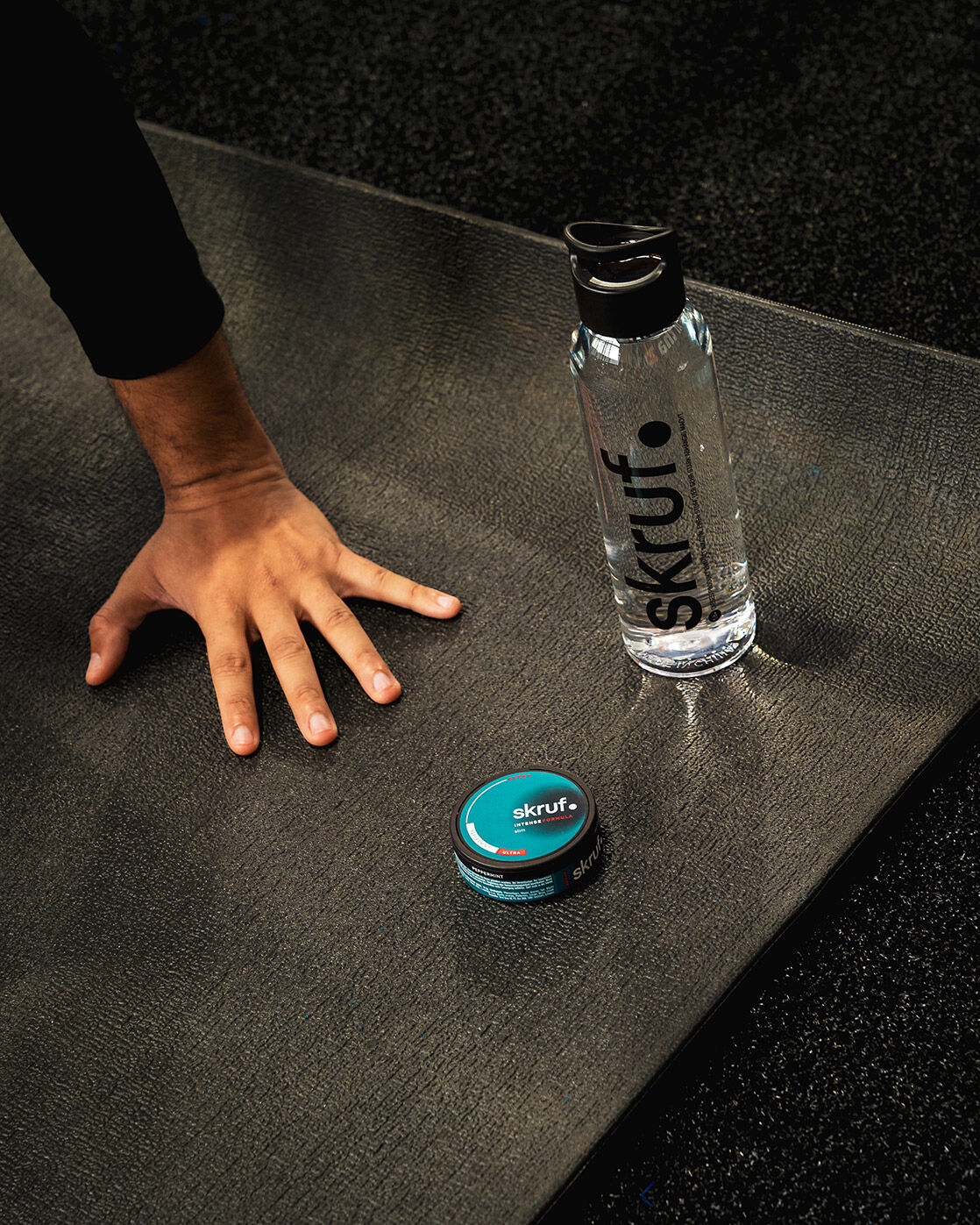 skruf Nikotinbeutel Dose neben einer skruf Wasserflasche, die zusammen auf einer Yogamatte liegen