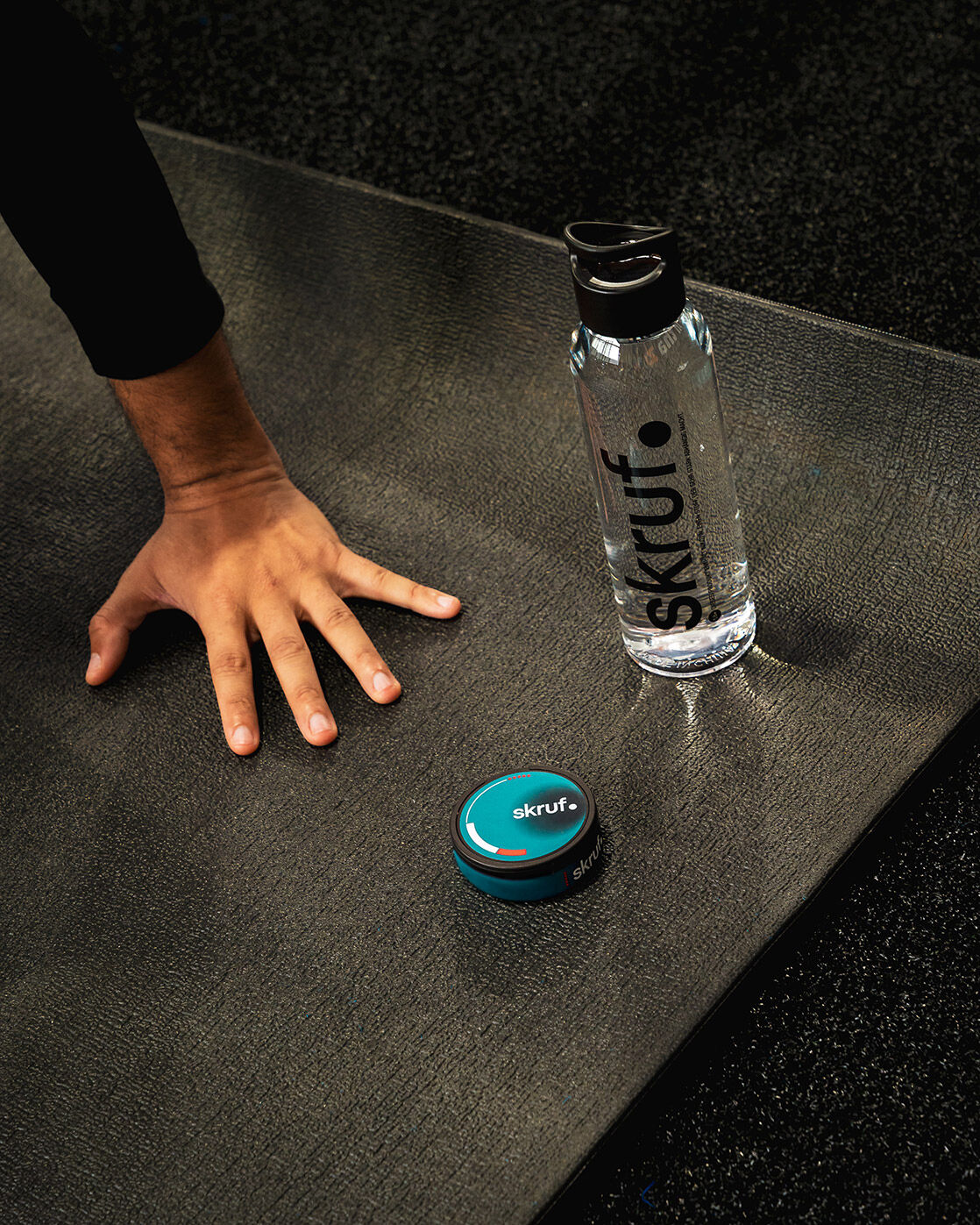 skruf Nikotinbeutel Dose neben einer skruf Wasserflasche, die zusammen auf einer Yogamatte liegen