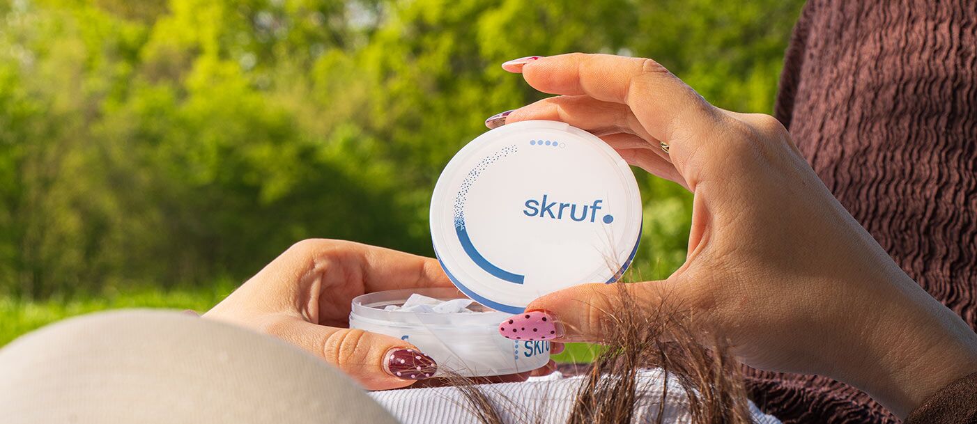 Person hält eine geöffnete Dose skruf Nikotinbeutel entspannt im Grünen.