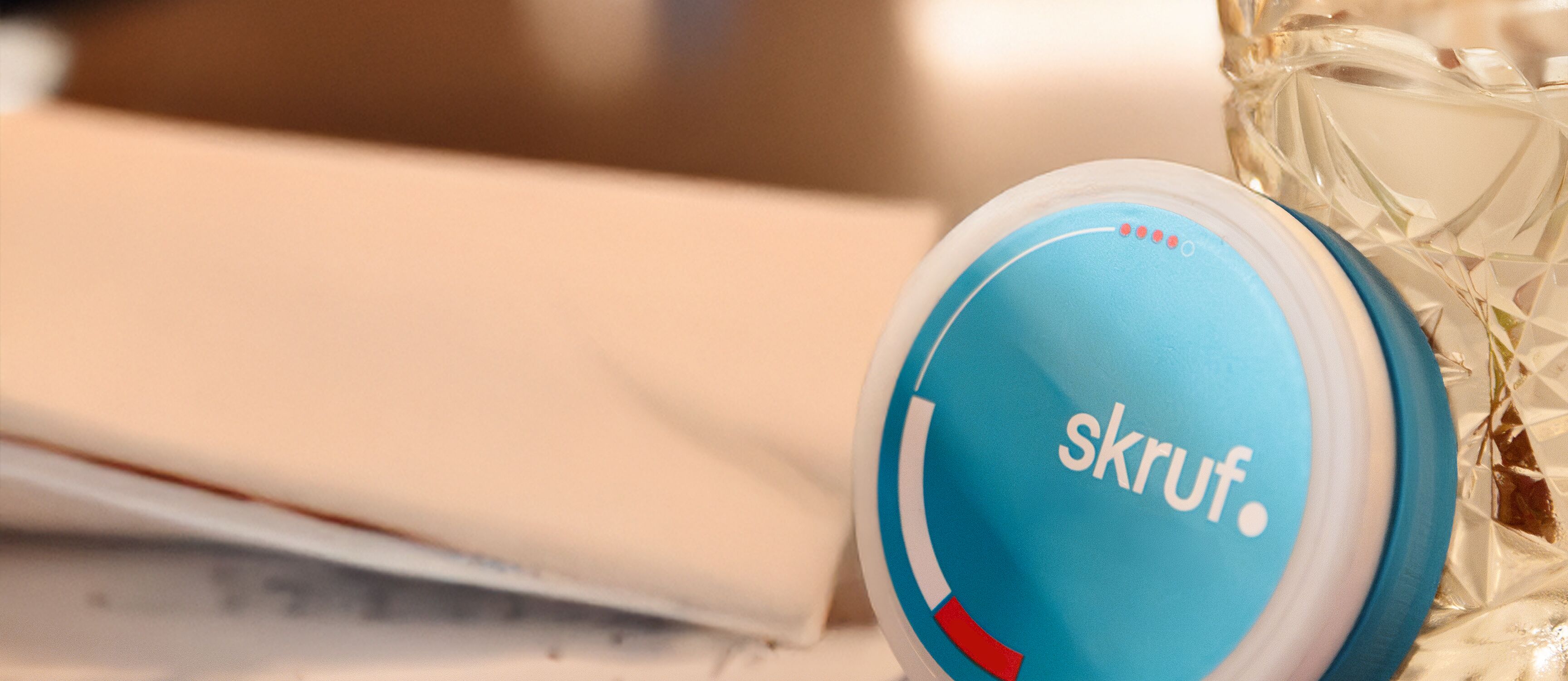 Blaue skruf.-Superwhite-Dose liegt neben Pizza und Getränk auf einem Tisch.