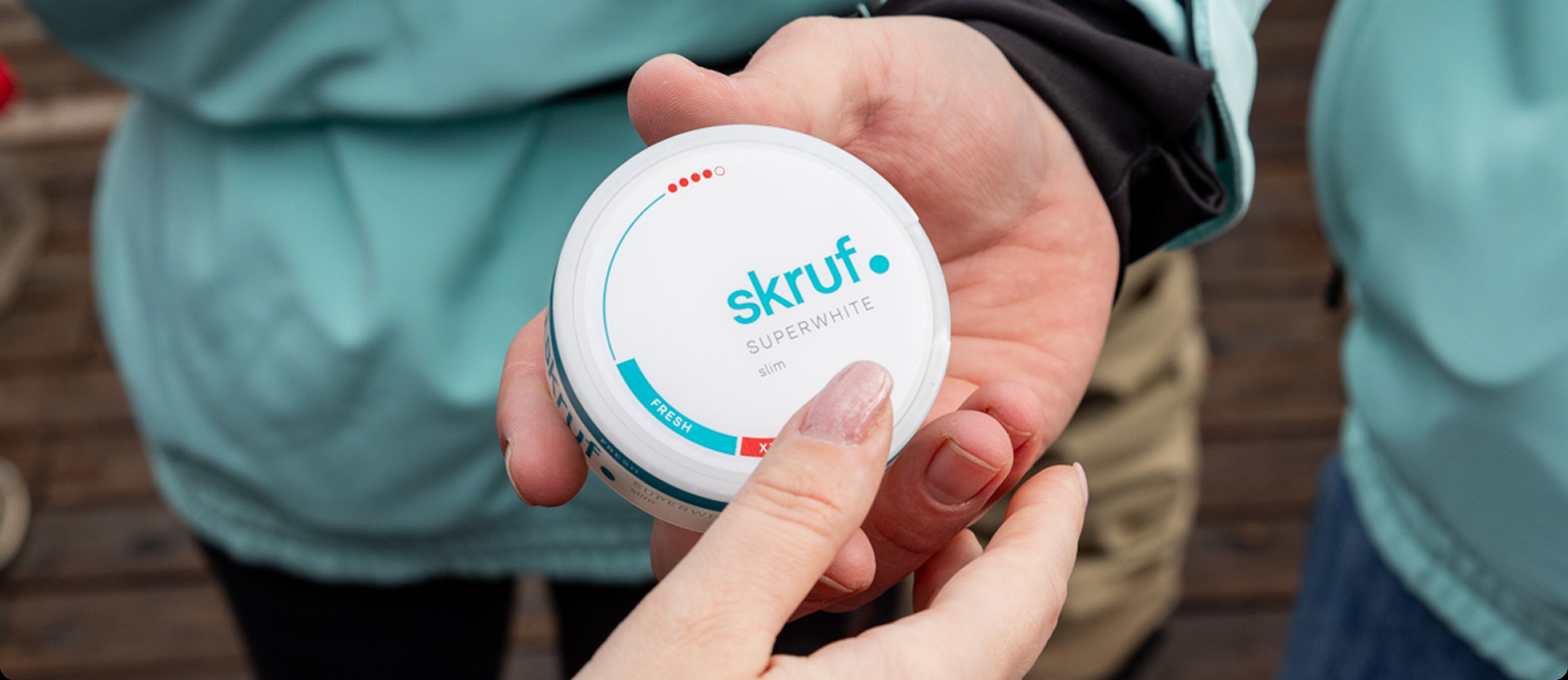 Hand übergibt weiße skruf.-Superwhite-Dose mit blauem Logo.